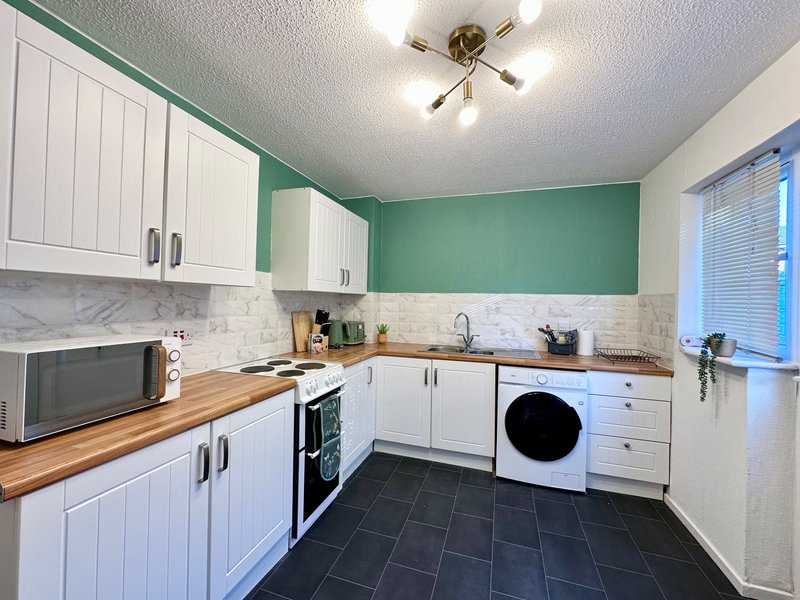 Modern kitchen with white cabinetry, green accent wall, wooden countertops and black floor tiles