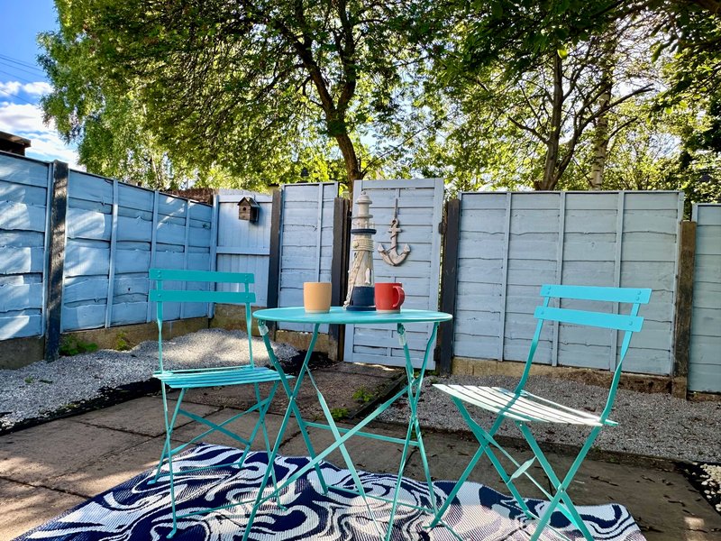 Outdoor garden seating area with turquoise chairs, table, and grey storage fence