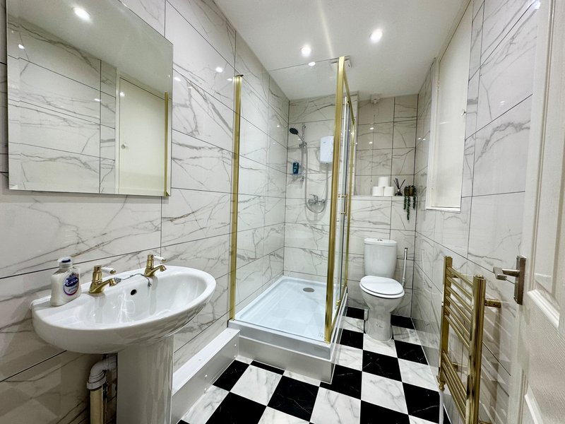 Modern bathroom with marble-effect tiles, white sink, shower cubicle and black-white floor tiles