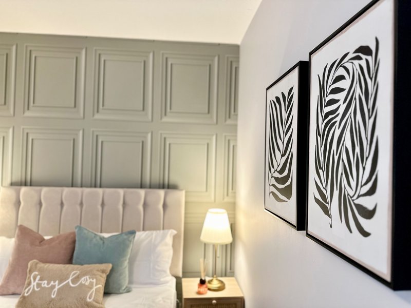 Modern bedroom with upholstered headboard, colorful pillows, bedside lamp, and abstract wall art