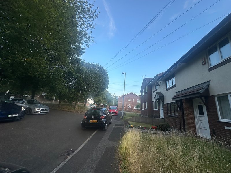 Street view of residential property with parked cars, terraced houses, and tree-lined road