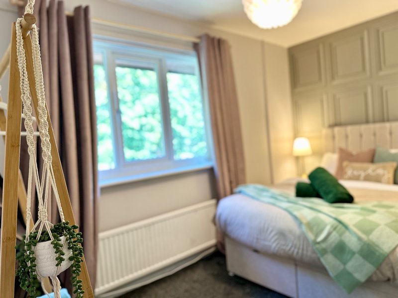 Bright bedroom with double bed, green bedding, large window with curtains, and wall-mounted lights