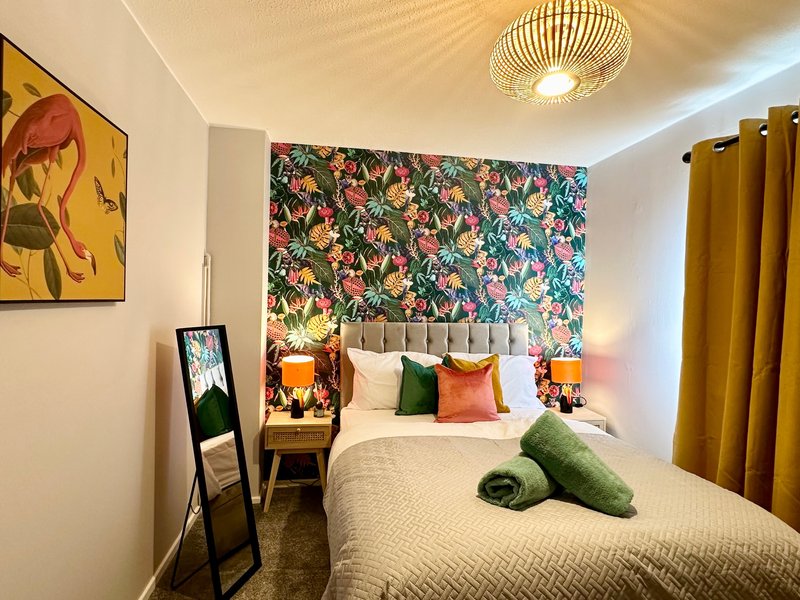 Modern bedroom with double bed, colorful floral accent wall, green towels and decorative pillows