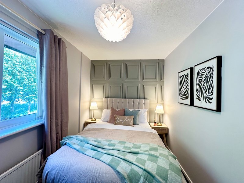 Compact bedroom with double bed, green headboard, pendant light and framed wall art