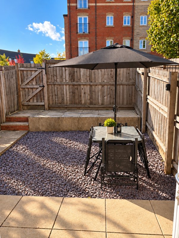 Courtyard patio with umbrella, table, wooden fencing and brick building backdrop