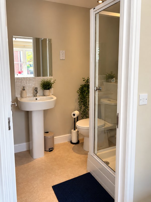 Clean bathroom with pedestal sink, mirror, toilet, and shower enclosure with plants