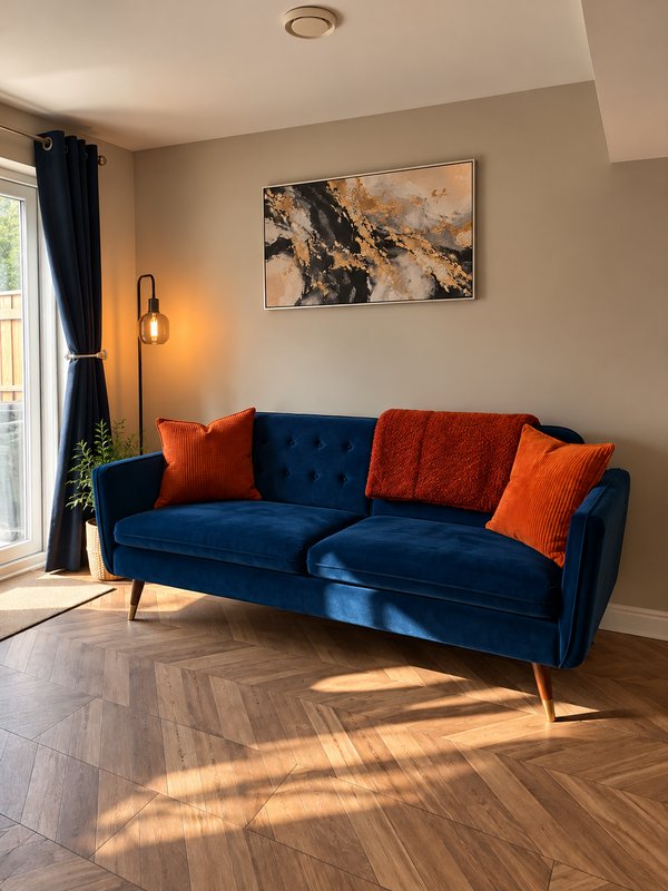 Modern living room with blue velvet sofa, orange cushions, wooden floor and wall art