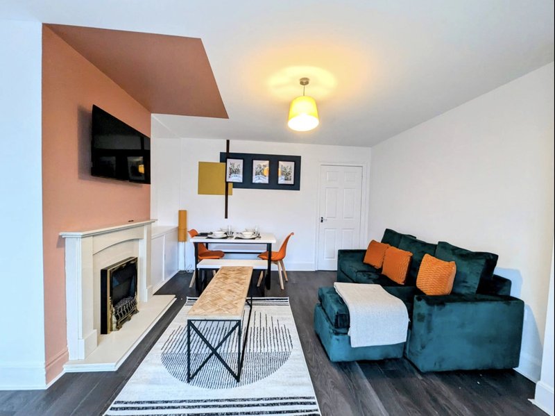 Open-plan living room with fireplace, dining table, teal sofa and orange accents