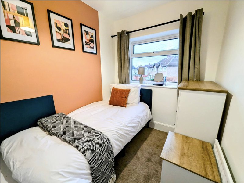 Bedroom with two single beds, orange accent wall, framed artwork and window with green curtains