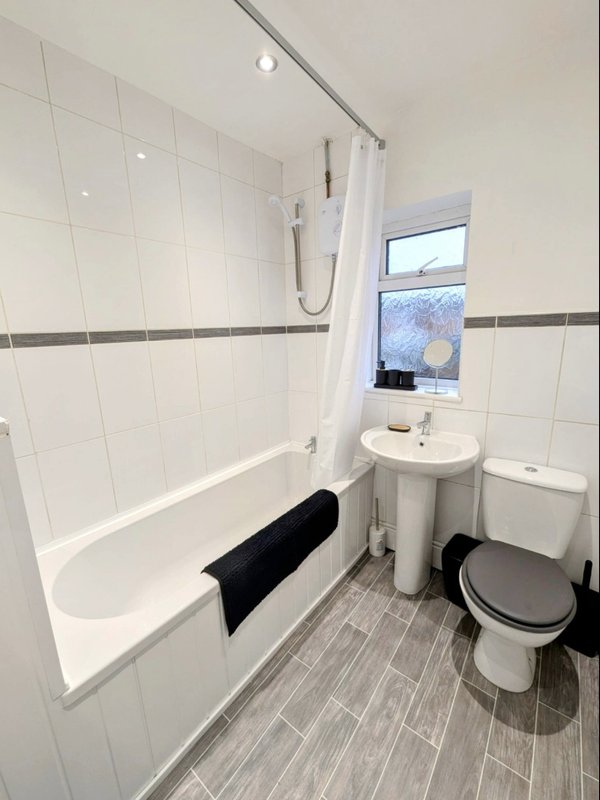 Clean bathroom with white tile walls, bathtub with shower curtain, pedestal sink and toilet