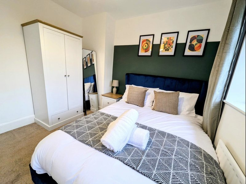 Modern bedroom with double bed, green headboard, white wardrobe, framed artwork and natural light from window