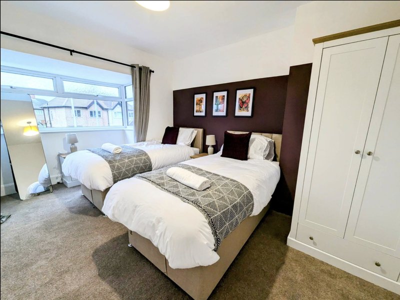 Modern bedroom with two single beds, dark headboard, white wardrobes and window view