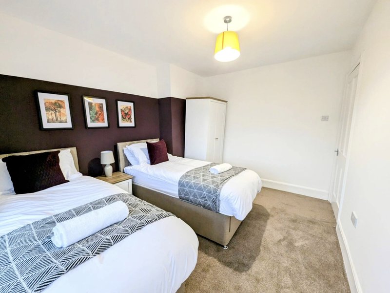 Twin bedroom with two single beds, purple accent wall, framed artwork and yellow ceiling light