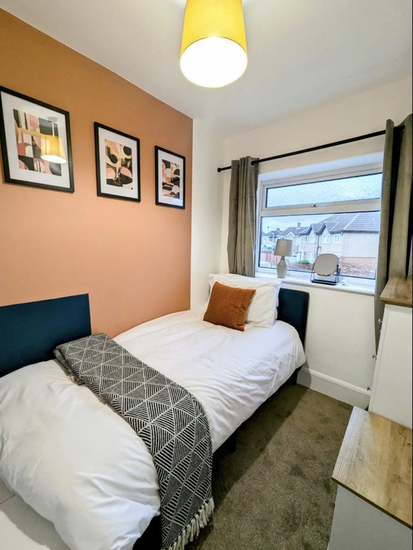 Compact bedroom with single bed, orange accent wall, yellow ceiling light, and window view
