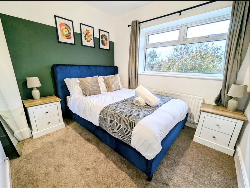 Bedroom with blue upholstered bed, green accent wall, white bedside tables, and large window
