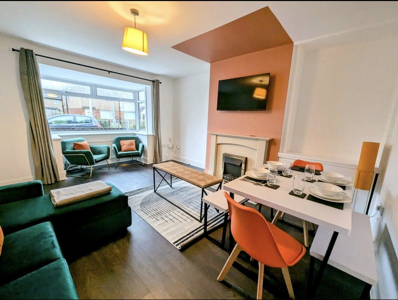 Open-plan living space with green sofa, dining table, desk area, and street-facing windows