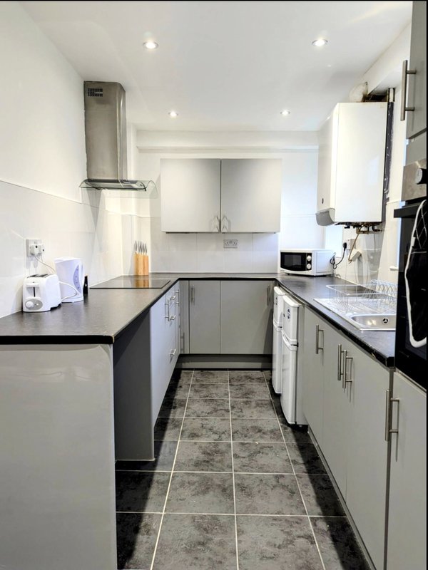 Modern galley kitchen with white cabinets, black countertops, stainless steel appliances and tiled flooring