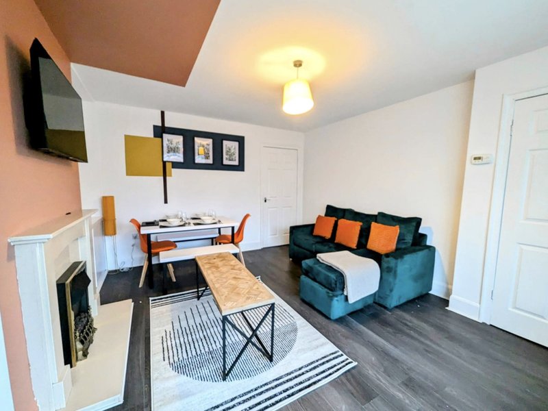 Open-plan living area with sofa, desk, dining table and mounted TV