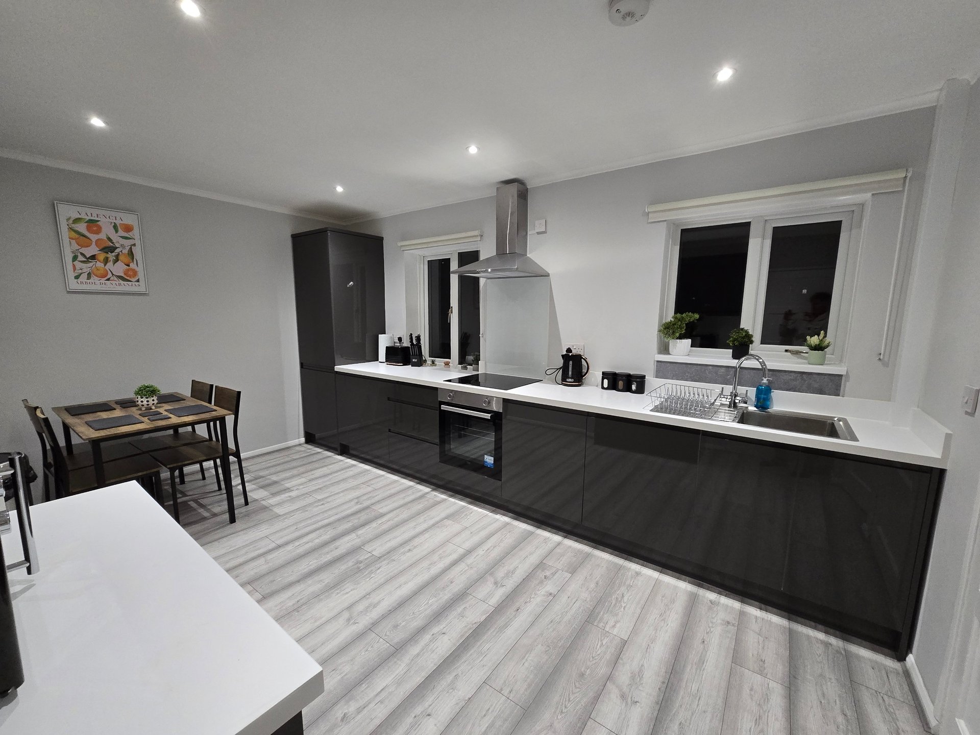Modern open-plan kitchen and dining area with black cabinetry, white countertops, and wood-effect flooring