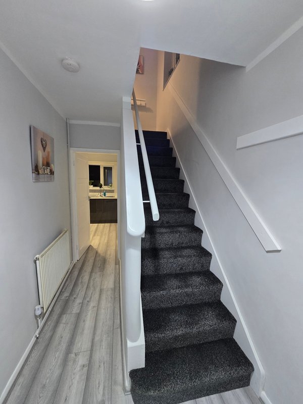 Bright hallway with staircase, gray carpet, white walls and wooden flooring
