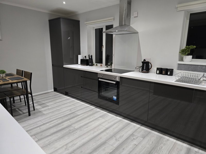 Modern kitchen with black cabinetry, white countertop, integrated appliances and striped flooring