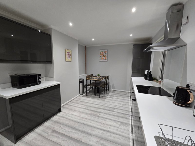 Modern open-plan kitchen and dining area with black and white cabinetry, dining table and stainless steel extractor hood