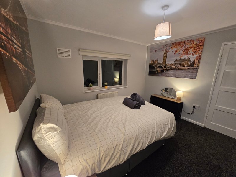Bedroom with double bed, white bedding, dark headboard, pendant light, wall art