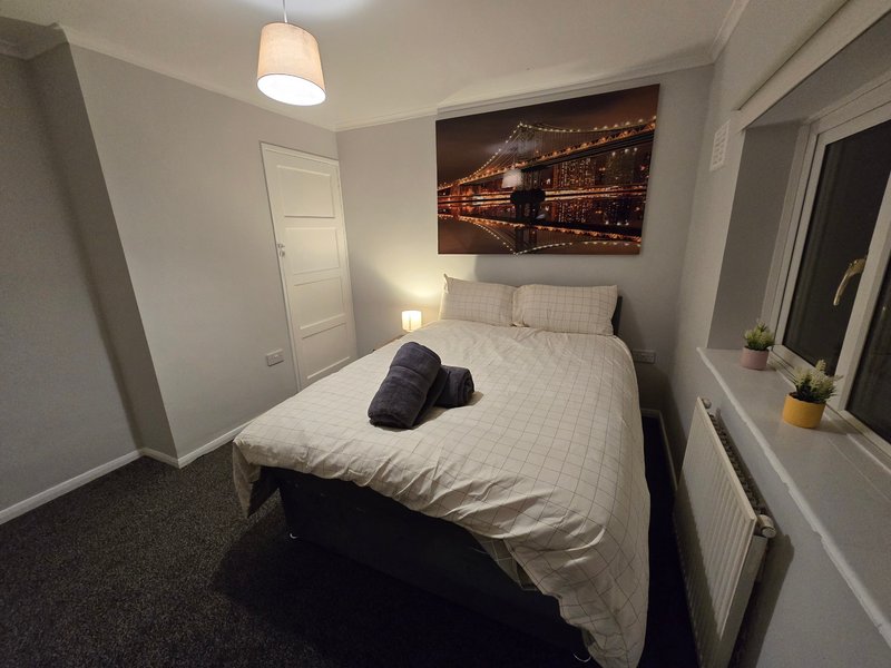 Bedroom with double bed, white bedding, pendant light, and city nightscape wall art