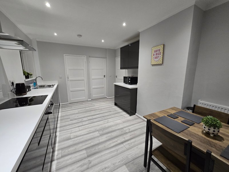 Modern kitchen and dining area with white cabinetry, wooden table, and grey flooring