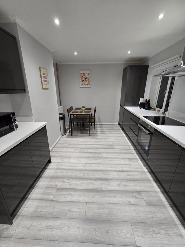 Modern galley kitchen with black cabinetry, white countertops, and dining area beyond