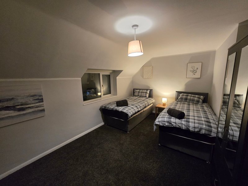 Shared bedroom with two single beds, dark carpet, pendant light, and wall-mounted shelving