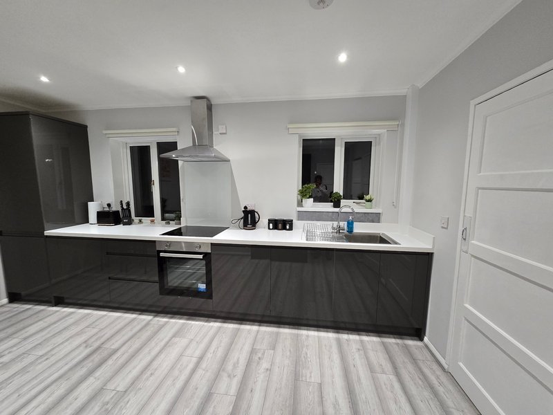 Modern open-plan kitchen with black cabinetry, white worktops, stainless steel extractor hood