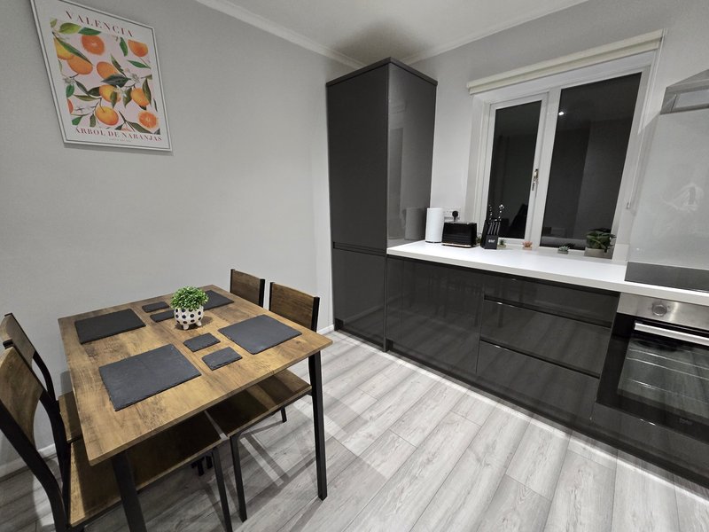Modern kitchen diner with wooden table, black chairs, dark cabinetry and striped flooring