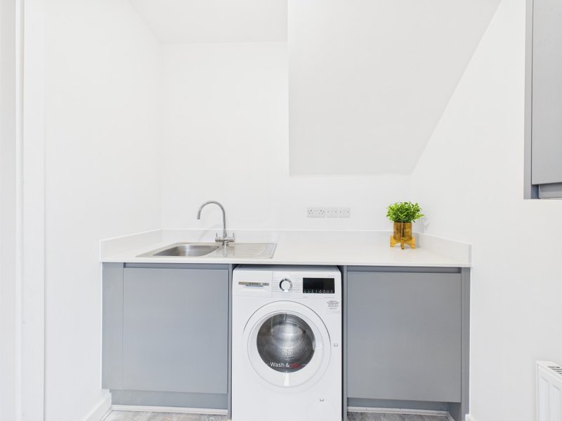 Modern laundry room with integrated washing machine, sink and grey cabinetry