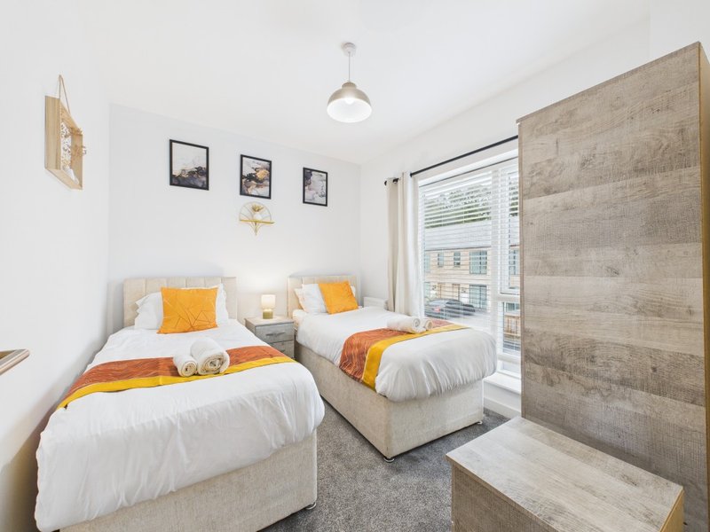 Twin bedroom with white beds, orange cushions, wooden wall paneling and window