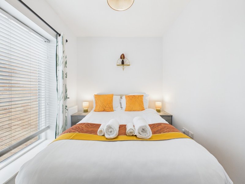 Bright bedroom with double bed, orange and white bedding, rolled towels, and window blinds