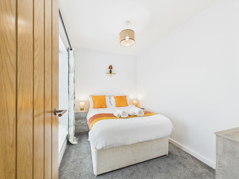 Modern bedroom with double bed, orange cushions, wooden wardrobe and ceiling light
