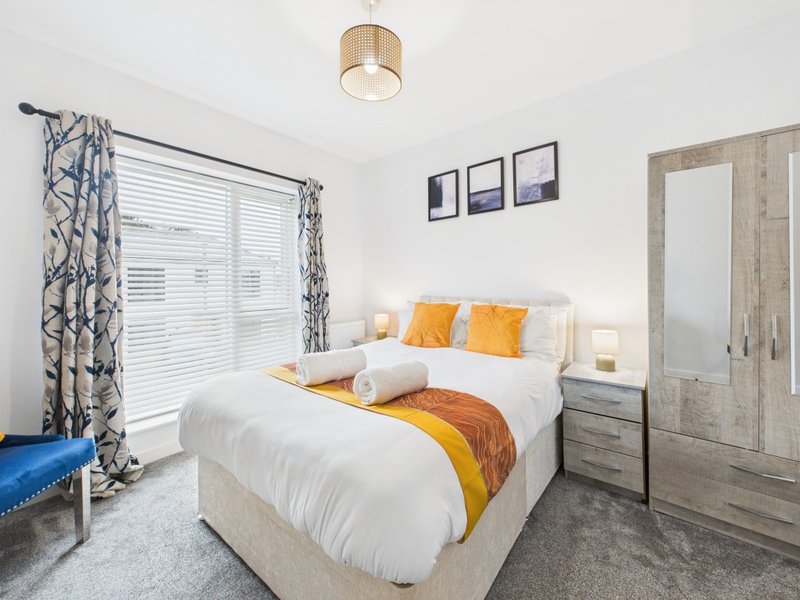 Modern bedroom with double bed, yellow and orange accents, wooden wardrobe and mirror
