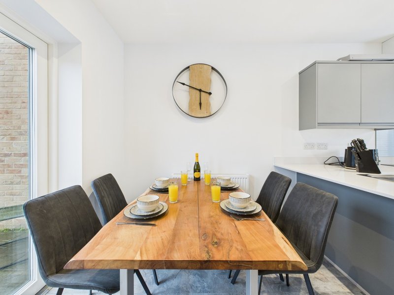 Dining area with wooden table, dark chairs, place settings, and kitchen beyond