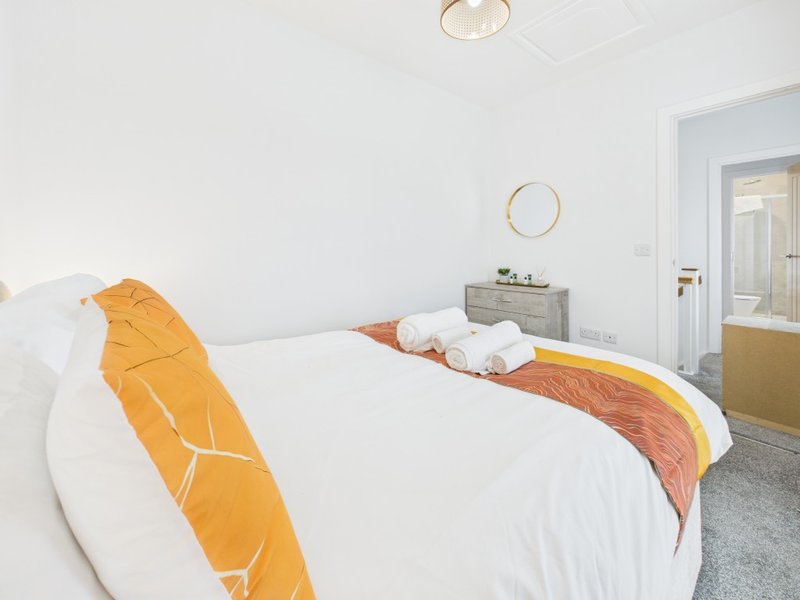 Modern bedroom with double bed, orange throw, white bedding, and en-suite bathroom visible