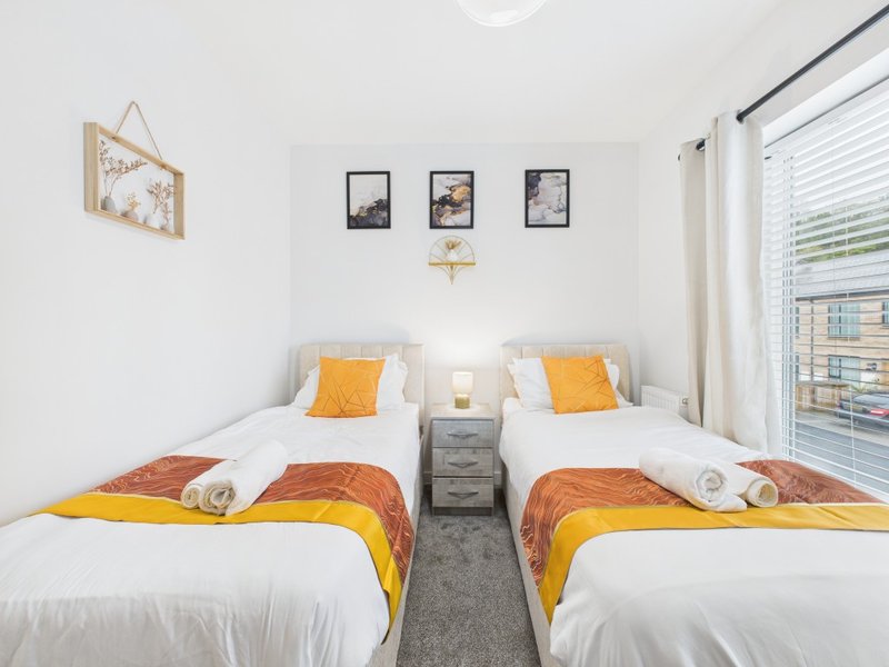 Bright twin bedroom with two single beds, orange and yellow bedding, framed wall art, and window with blinds