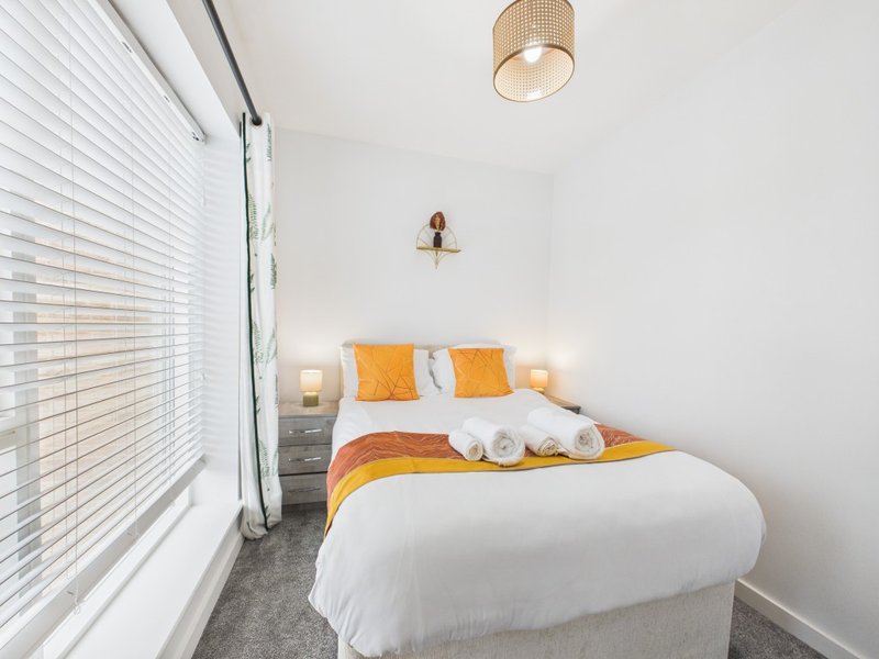 Modern bedroom with double bed, orange bedding, white pillows, and pendant ceiling light