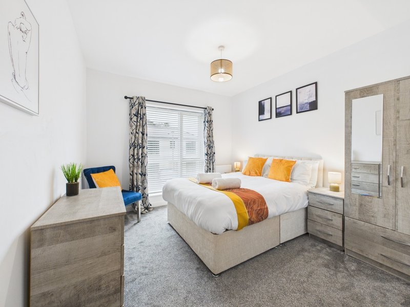 Modern bedroom with double bed, wooden furniture, yellow and orange cushions, and window with curtains