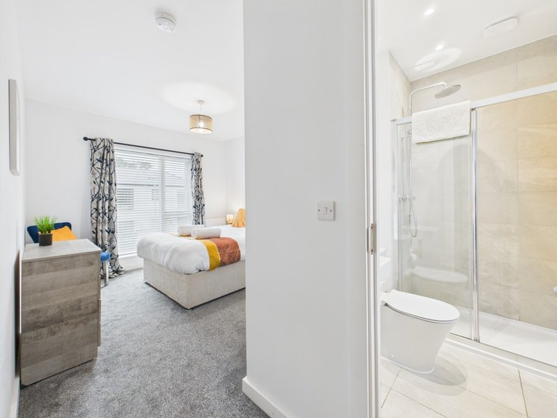 Bright bedroom with double bed, wooden dresser, ensuite bathroom visible through open door