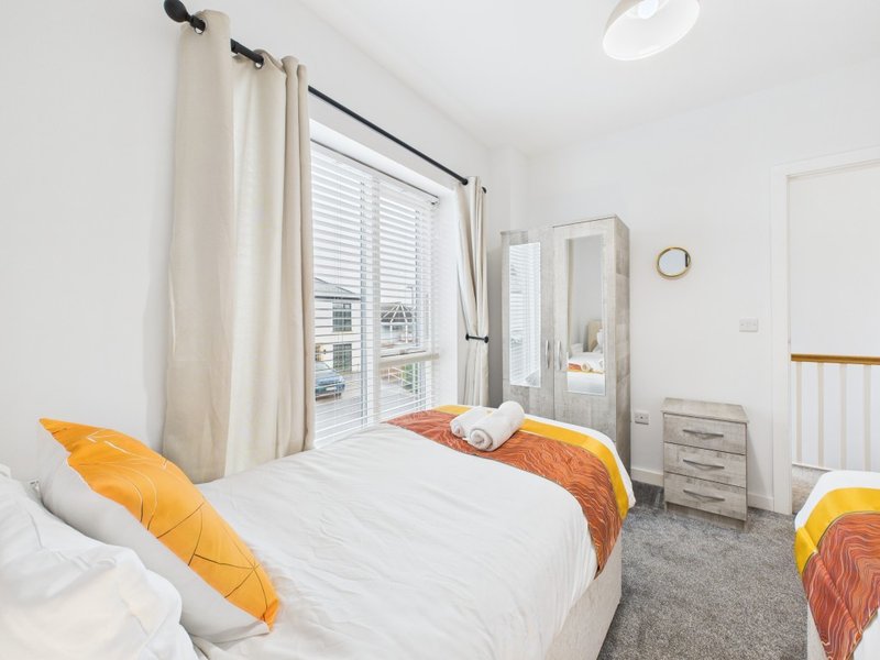 Bright bedroom with double bed, orange cushions, patio doors and wooden wardrobe