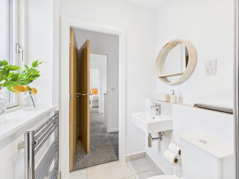 Clean modern bathroom with white walls, round mirror, sink, toilet and wooden door