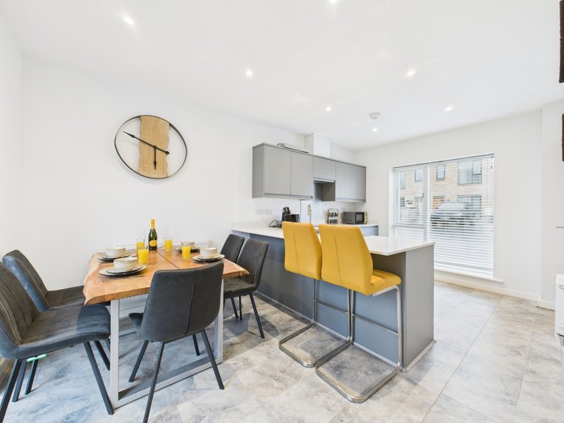 Open-plan kitchen and dining area with yellow bar stools, wooden table, and modern appliances