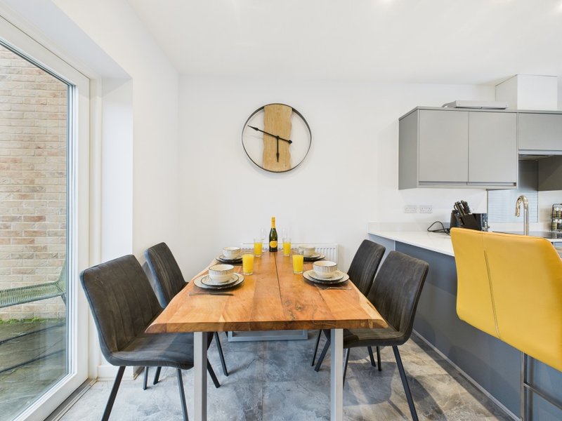 Modern dining room with wooden table, black chairs, wall clock and kitchen cabinets