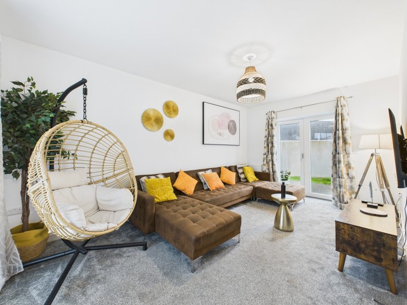 Modern living room with hanging egg chair, brown sofa, yellow cushions and glass doors to garden