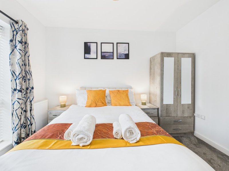 Modern bedroom with double bed, rolled towels, yellow throw and orange pillows